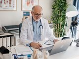 Male physician sitting at a desk in front of a computer.